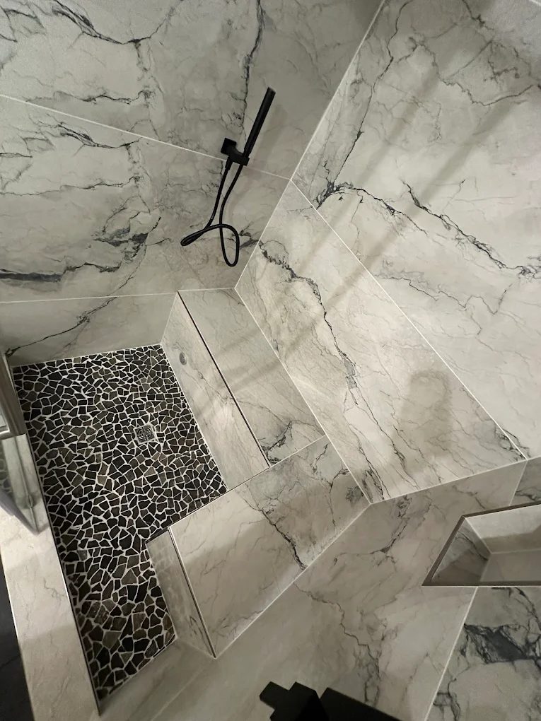 Custom marble walk-in shower with pebble floor and built-in bench by NoBull Man